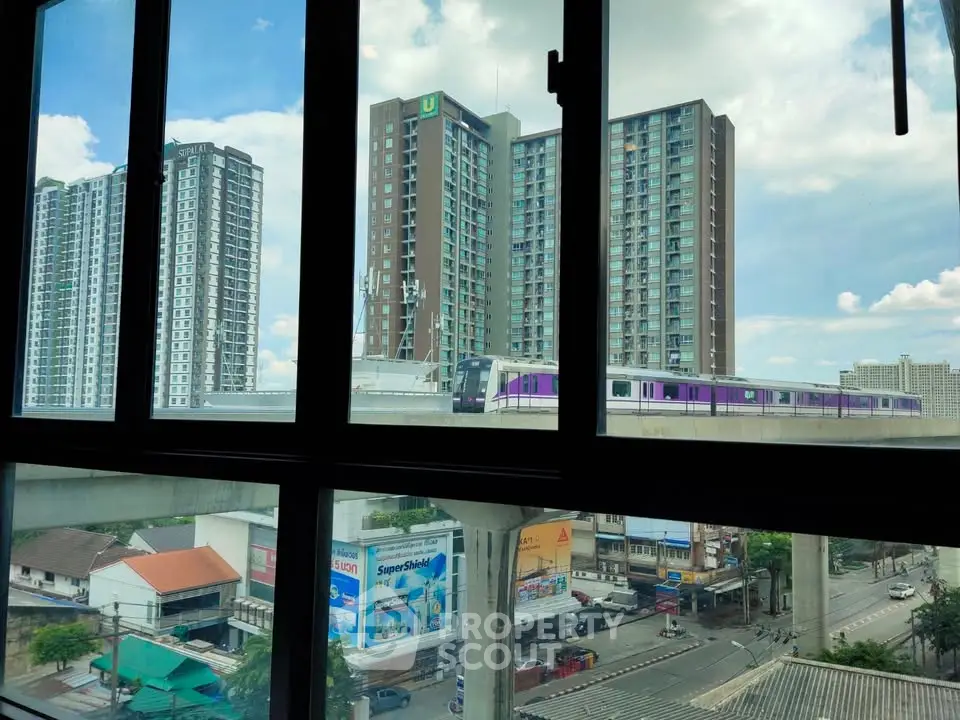 Urban view from window showcasing modern high-rise buildings and cityscape with train passing by.