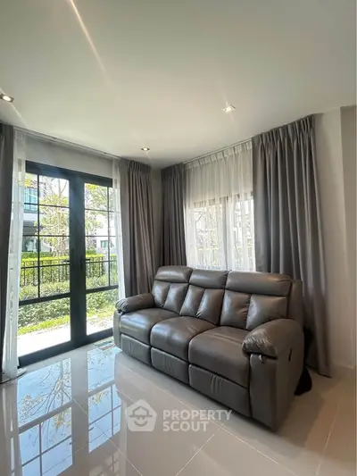 Spacious living room with modern leather sofa and large windows offering garden view.