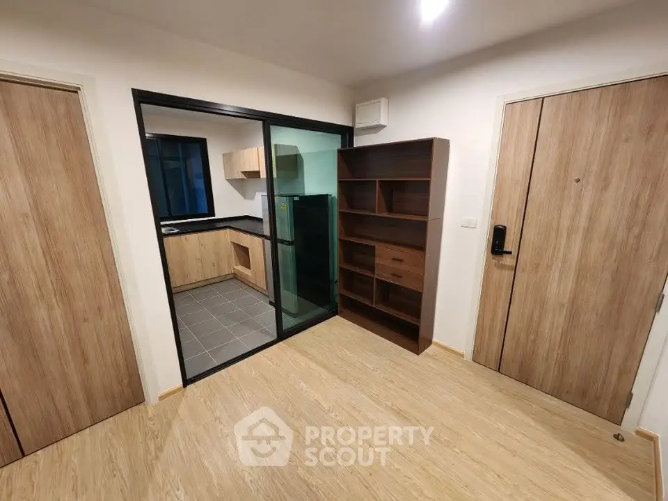 Modern apartment interior with open kitchen and wooden flooring, featuring sleek cabinetry and a glass partition.