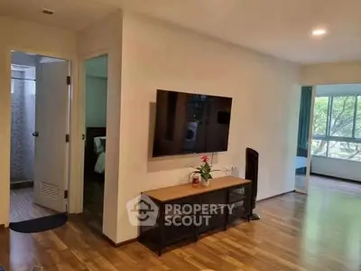 Spacious living room with wall-mounted TV and wooden flooring, adjacent to a cozy bedroom.