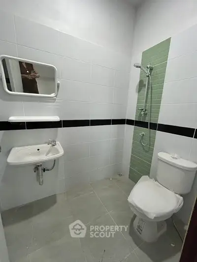 Modern bathroom with sleek white tiles and green accent wall, featuring a shower and toilet.