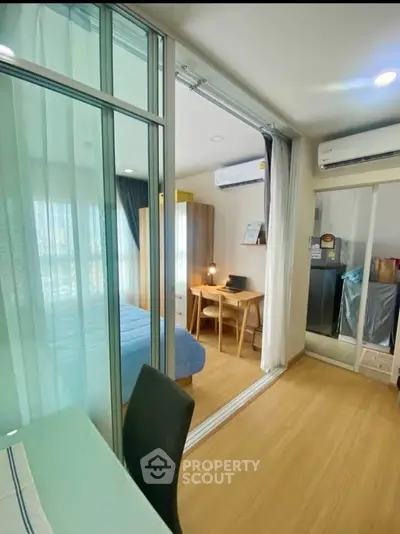 Modern apartment interior with sliding glass doors, cozy bedroom, and study area, featuring wooden flooring and ample natural light.