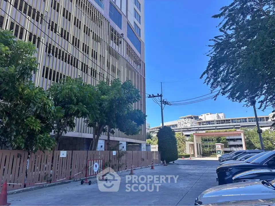 Modern building exterior with parking area and lush greenery under a clear blue sky.