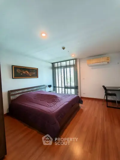Spacious bedroom with wooden flooring and large window in modern apartment