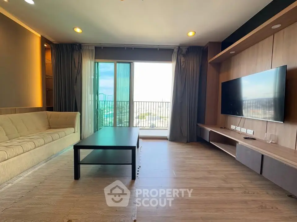 Spacious modern living room with large window and city view, featuring sleek furniture and wooden flooring.