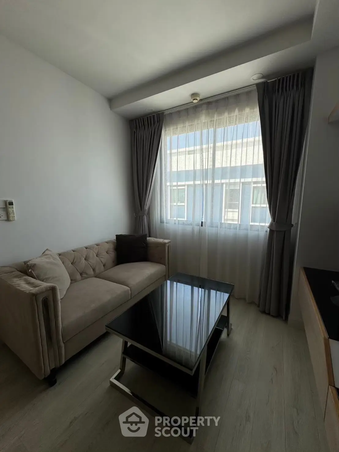 Modern living room with stylish sofa and glass coffee table, featuring large window with elegant curtains.