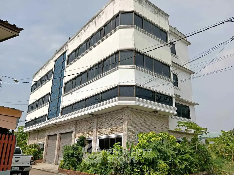 Modern multi-story building with large windows and lush greenery, ideal for commercial or residential use.