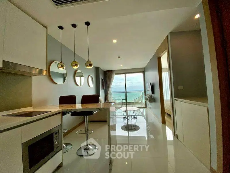 Modern open-layout kitchen and living room with ocean view balcony in luxury apartment.