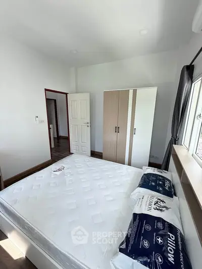 Modern bedroom with new mattress and wardrobe, bright natural light from large window.