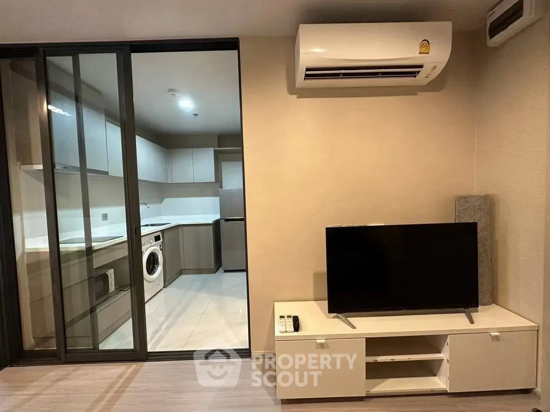 Modern living room with sliding glass doors to a sleek kitchen featuring a washing machine and air conditioning.