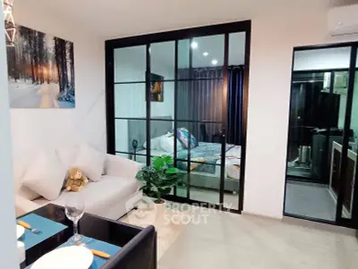 Modern living room with glass partition leading to a cozy bedroom, featuring elegant decor and dining setup.