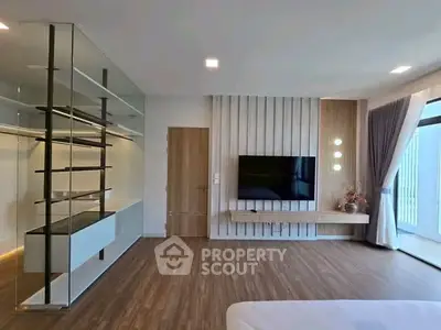 Modern living room with sleek glass shelving and wall-mounted TV, featuring elegant wood flooring and natural light.