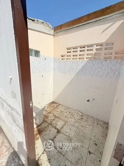 Unfinished bathroom with exposed ceiling and tiled walls in need of renovation.