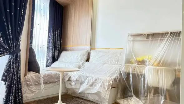 Modern living room with stylish furniture covered in protective plastic, elegant curtains, and a cozy atmosphere.