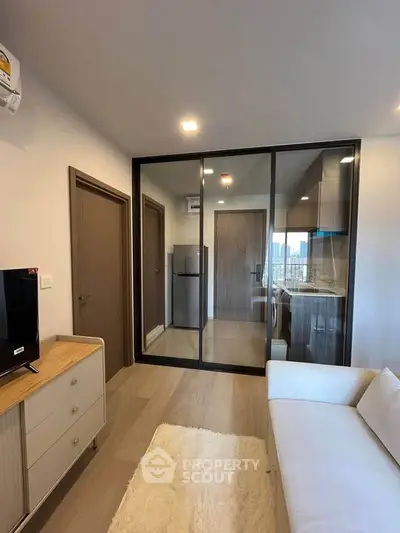 Modern living room with glass partition, cozy sofa, and sleek kitchen view.