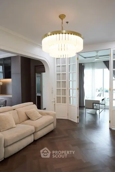 Elegant living room with chandelier and open layout leading to balcony with view.
