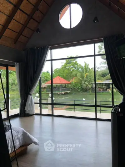 Stunning bedroom with floor-to-ceiling windows offering serene river views and lush greenery.