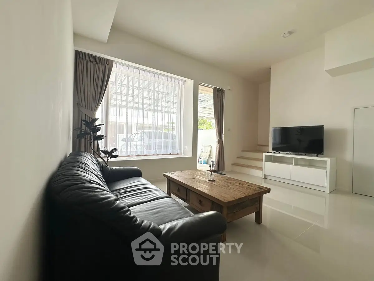 Spacious living room with sleek leather sofa and modern TV setup, perfect for relaxation.