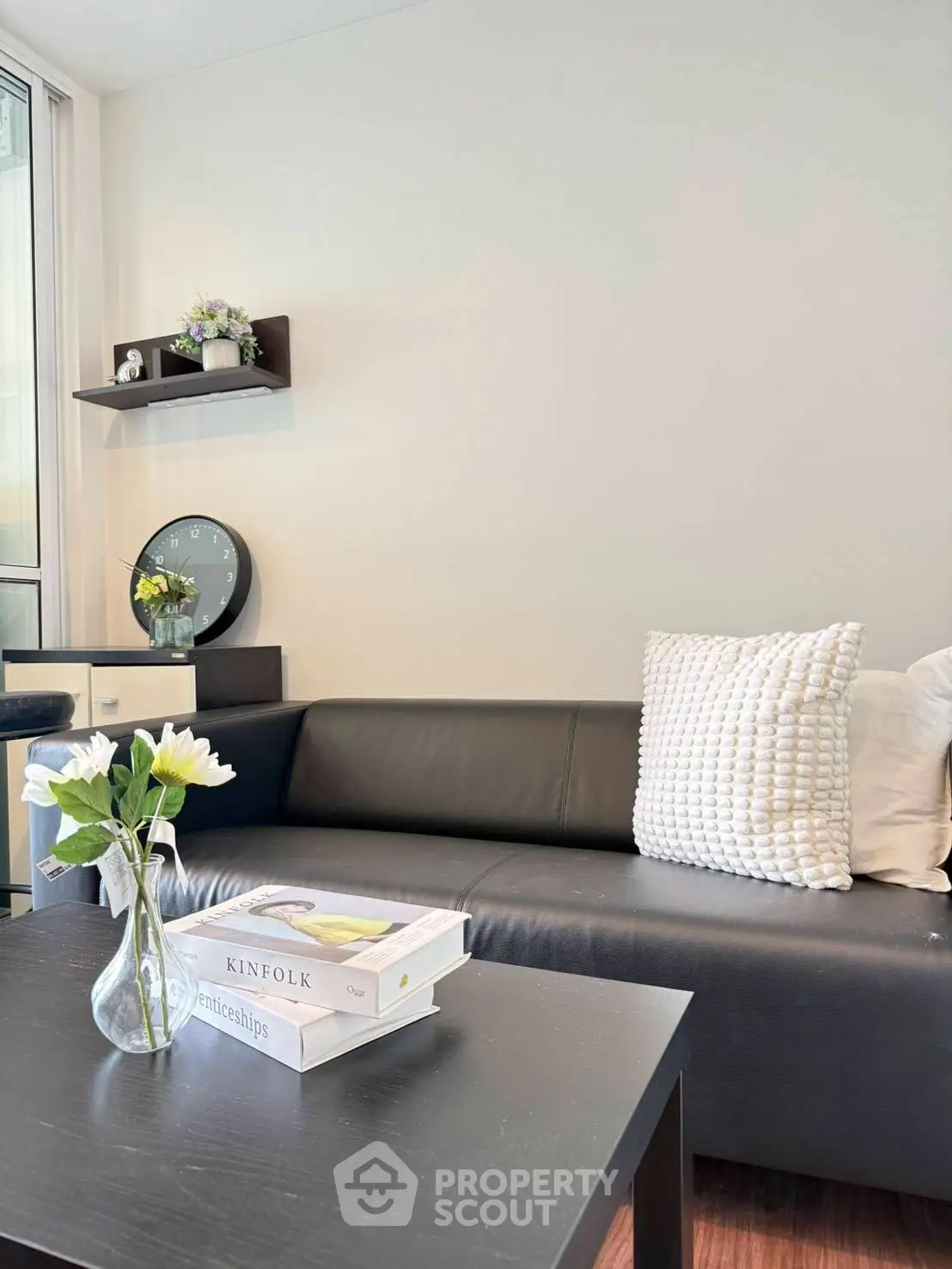Modern living room with sleek black sofa, decorative pillows, and stylish coffee table with books and flowers.