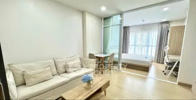 Modern open-plan living room with cozy sofa and adjacent bedroom, featuring elegant decor and natural light.