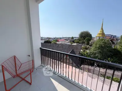 Spacious balcony with stunning city view and modern red chair, perfect for relaxation.
