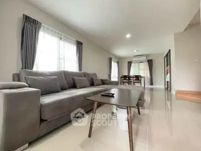 Spacious living room with modern gray sofa and dining area, featuring large windows and elegant curtains.