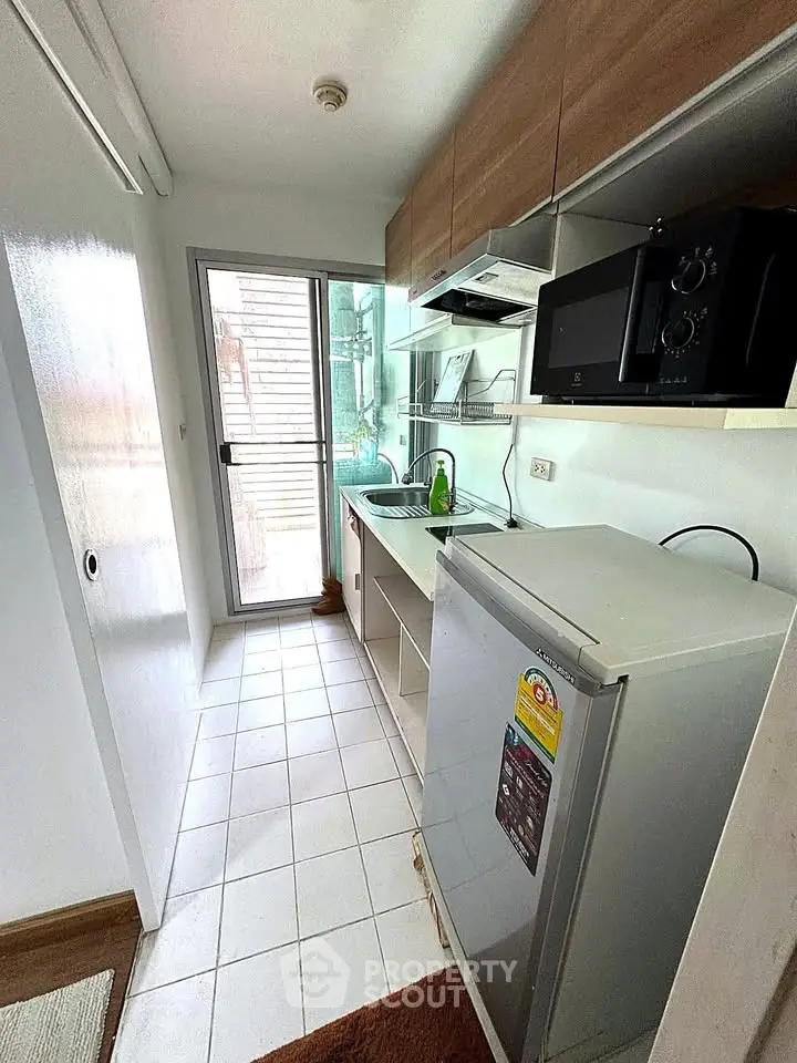 Compact kitchen with modern appliances and natural light, featuring a microwave and refrigerator.