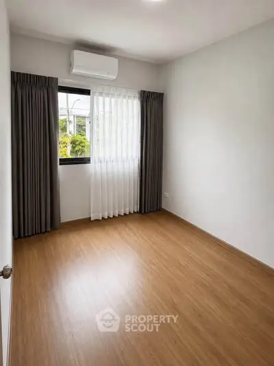 Spacious empty room with wooden flooring and large window, perfect for customization.