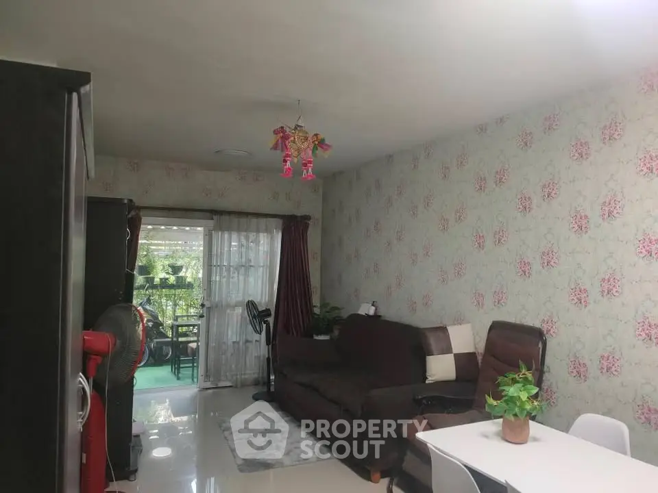Charming living room with floral wallpaper and cozy seating, opening to a lush balcony view.