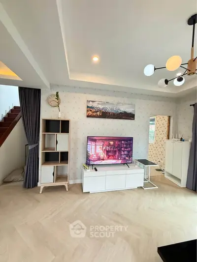Modern living room with stylish decor and staircase, featuring a flat-screen TV and elegant lighting.