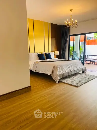 Spacious bedroom with elegant chandelier and balcony access, featuring modern decor and wooden flooring.