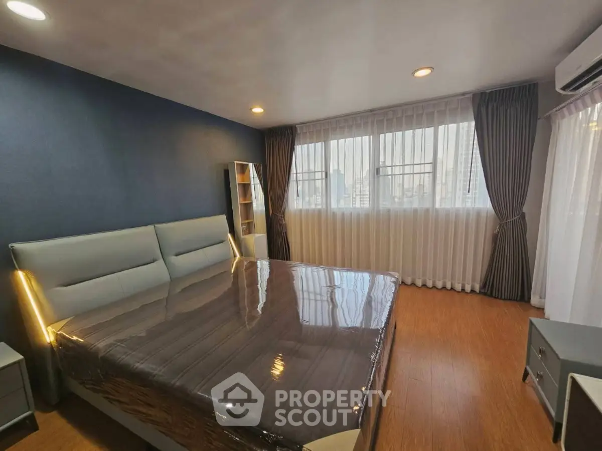 Spacious modern bedroom with large windows and elegant furnishings in a high-rise apartment.