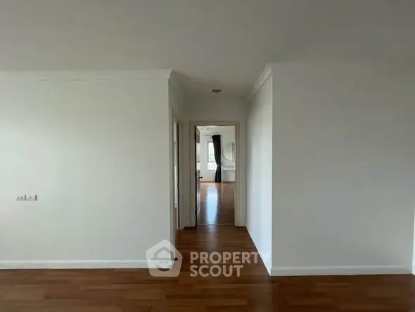 Spacious interior with wooden flooring and white walls, leading to a bright room.
