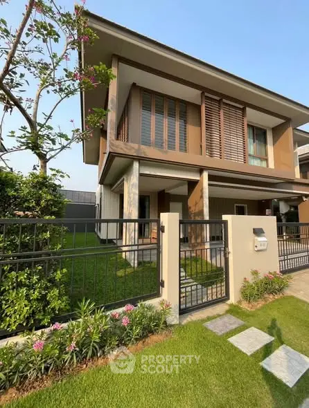 Modern two-story house with landscaped garden and gated entrance, showcasing contemporary architecture and lush greenery.