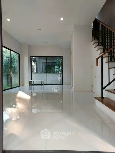 Spacious modern living room with large windows and sleek staircase, perfect for natural light lovers.