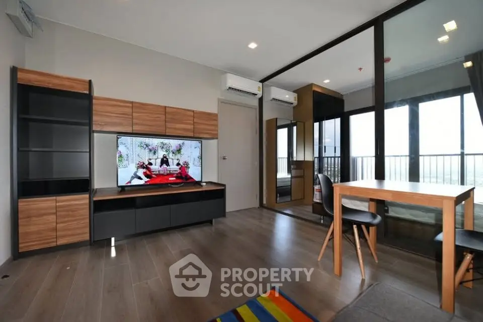 Modern living room with stylish furniture and large TV, featuring wooden flooring and balcony access.