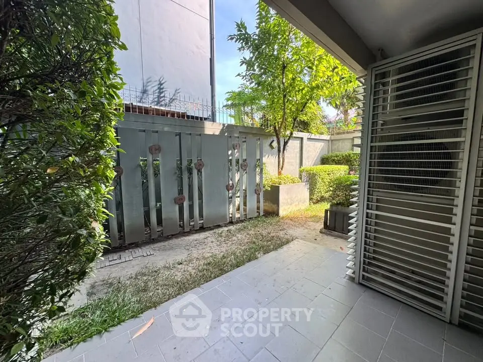 Charming garden view from a modern residential patio with lush greenery and sleek metal gate.
