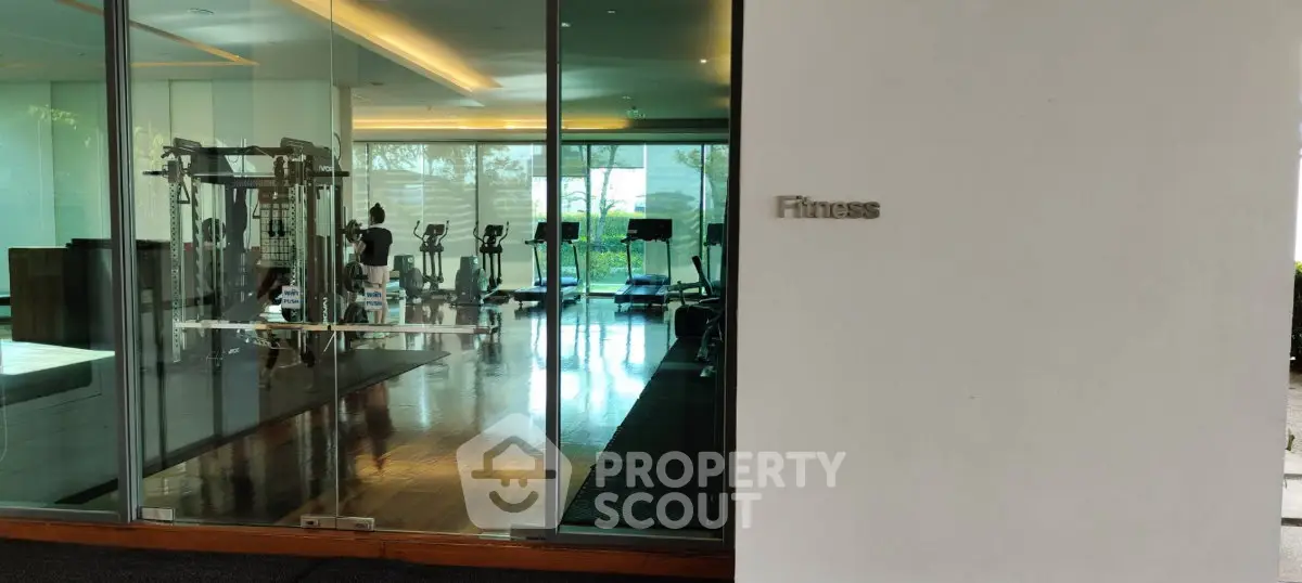 Modern fitness gym with glass walls and exercise equipment in luxury building.