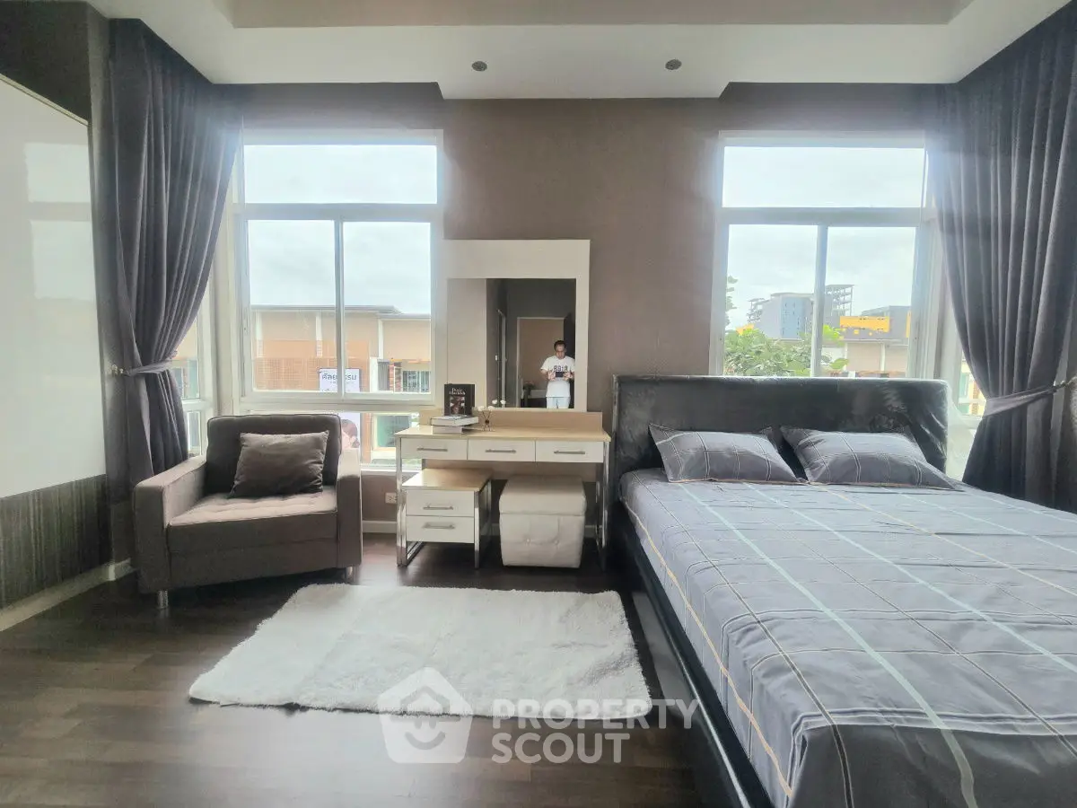 Spacious bedroom with large windows and modern decor, featuring a cozy armchair and stylish bed.