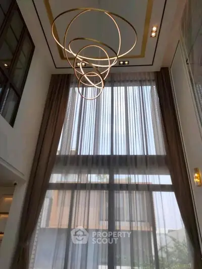 Luxurious high-ceiling living room with elegant chandelier and floor-to-ceiling windows.