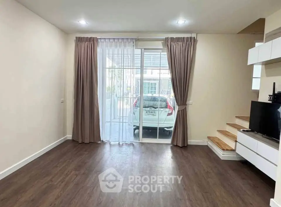 Spacious living room with wooden flooring and large window overlooking driveway.