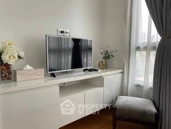 Modern living room with sleek TV setup and elegant decor, featuring large windows for natural light.