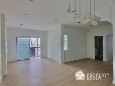 Spacious and bright living room with elegant hardwood floors and modern lighting fixtures, leading to a sunny outdoor area.