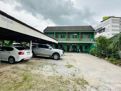Spacious two-story green building with ample parking space and covered carport, ideal for residential or commercial use.