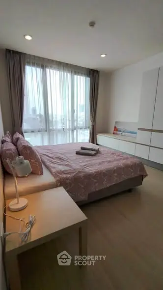 Spacious bedroom with large window and modern furnishings in a high-rise apartment.