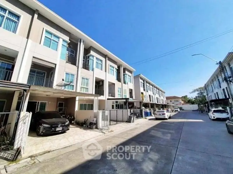 Modern townhouse complex with spacious parking and clear blue sky.