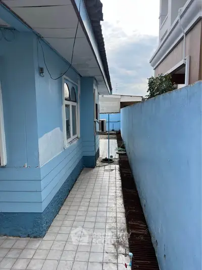 Charming exterior view of a blue house with tiled walkway and side wall, perfect for cozy living.