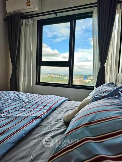 Cozy bedroom with stunning city view through large window, featuring striped bedding and elegant curtains.