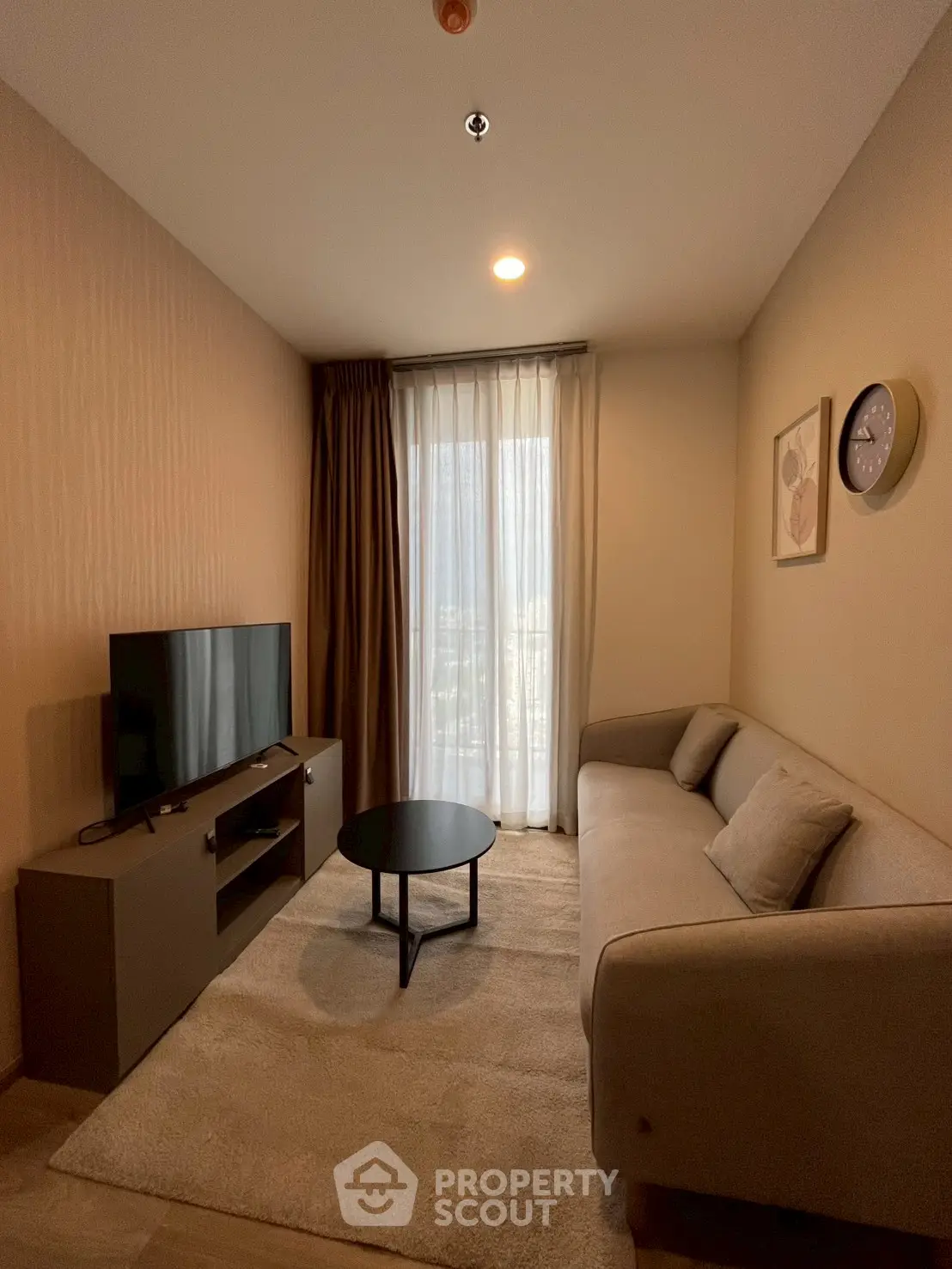 Cozy living room with modern sofa, TV, and natural light from large window.
