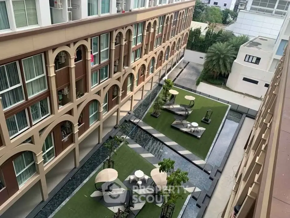 Modern apartment building with stylish courtyard featuring seating areas and greenery.